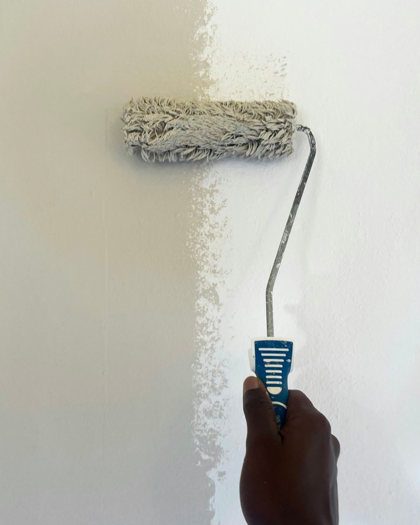 A paint roller putting a fresh coat of white paint on a wall