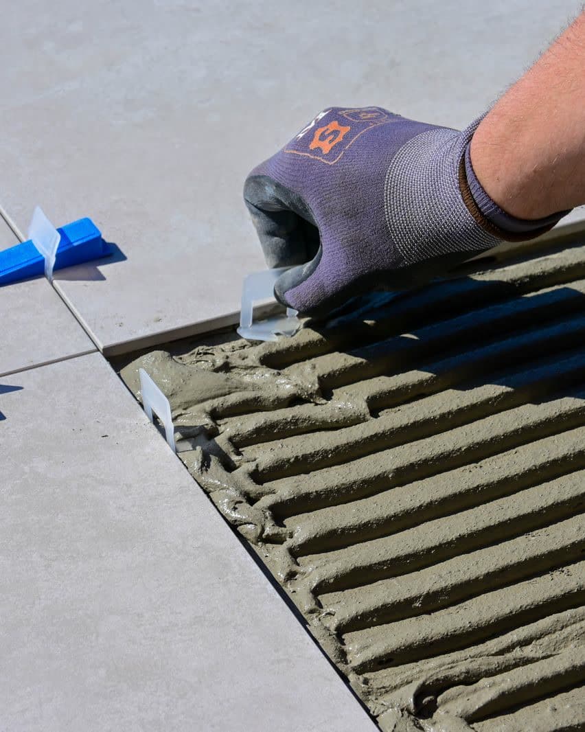 A gloved hand setting tile levelers between new floor tiles